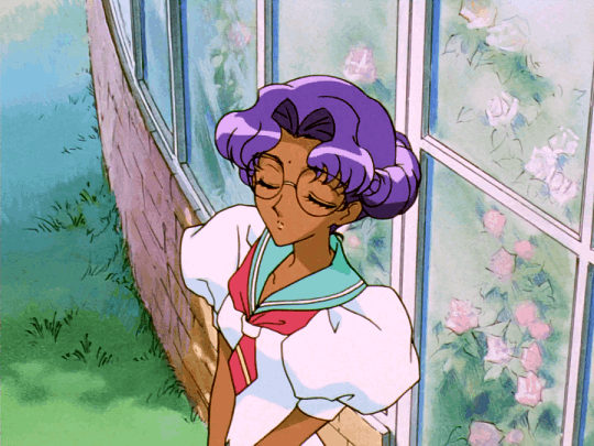 Anthy GIF. She has short purple hair curled around her face, medium brown skin, and green eyes. She wears large, round glasses and a white sailor-style school uniform.